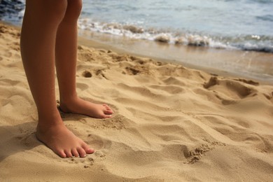 Photo of Little girl standing on sandy beach, closeup. Space for text