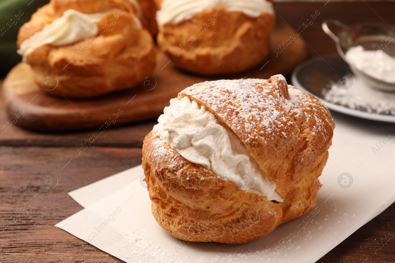 Photo of Delicious profiteroles with cream filling and powdered sugar on wooden table, closeup