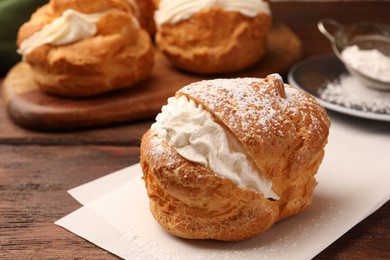 Photo of Delicious profiteroles with cream filling and powdered sugar on wooden table, closeup