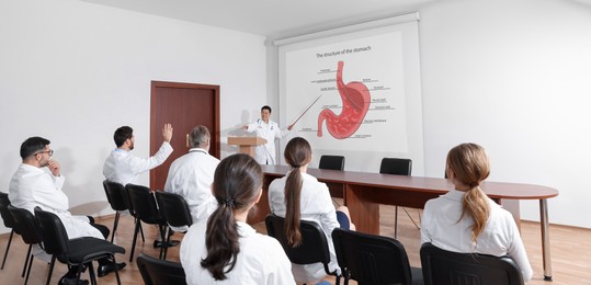 Image of Lecture in gastroenterology. Professors and doctors in conference room. Projection screen with structure of stomach