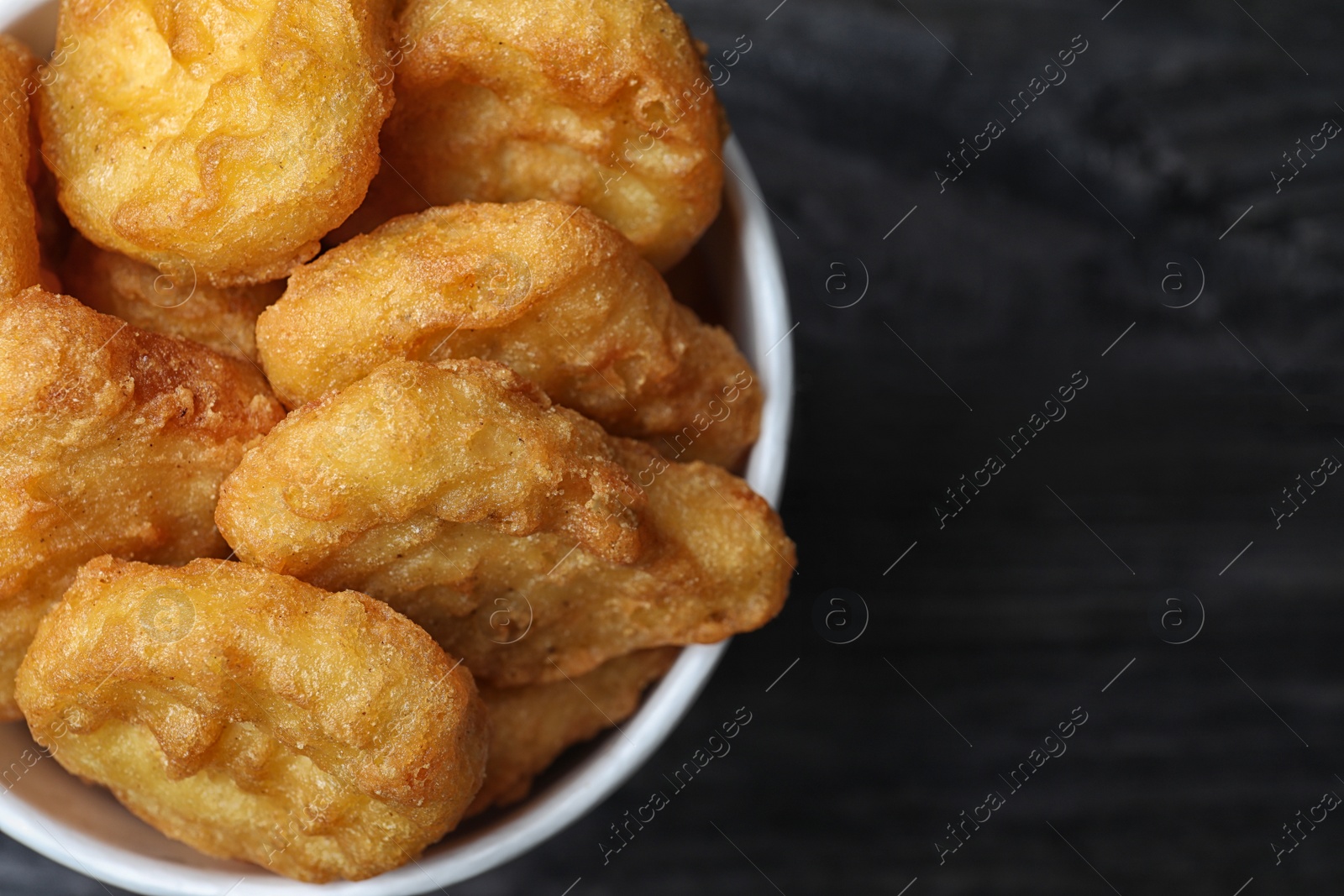 Photo of Bucket with tasty chicken nuggets on black wooden table, top view