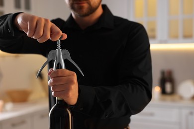 Photo of Man opening wine bottle with corkscrew indoors, closeup