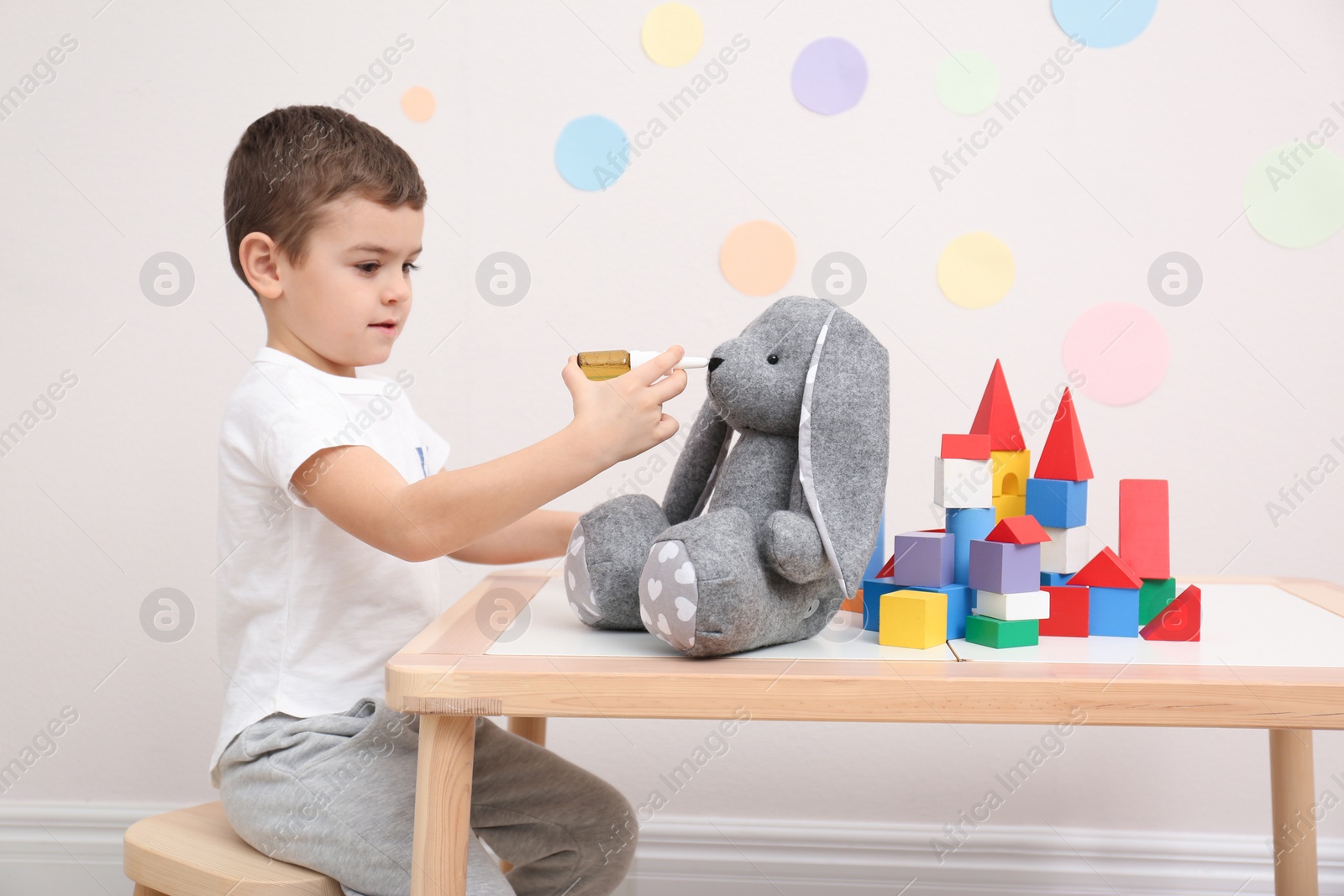 Photo of Cute child playing doctor with stuffed toy at table in hospital