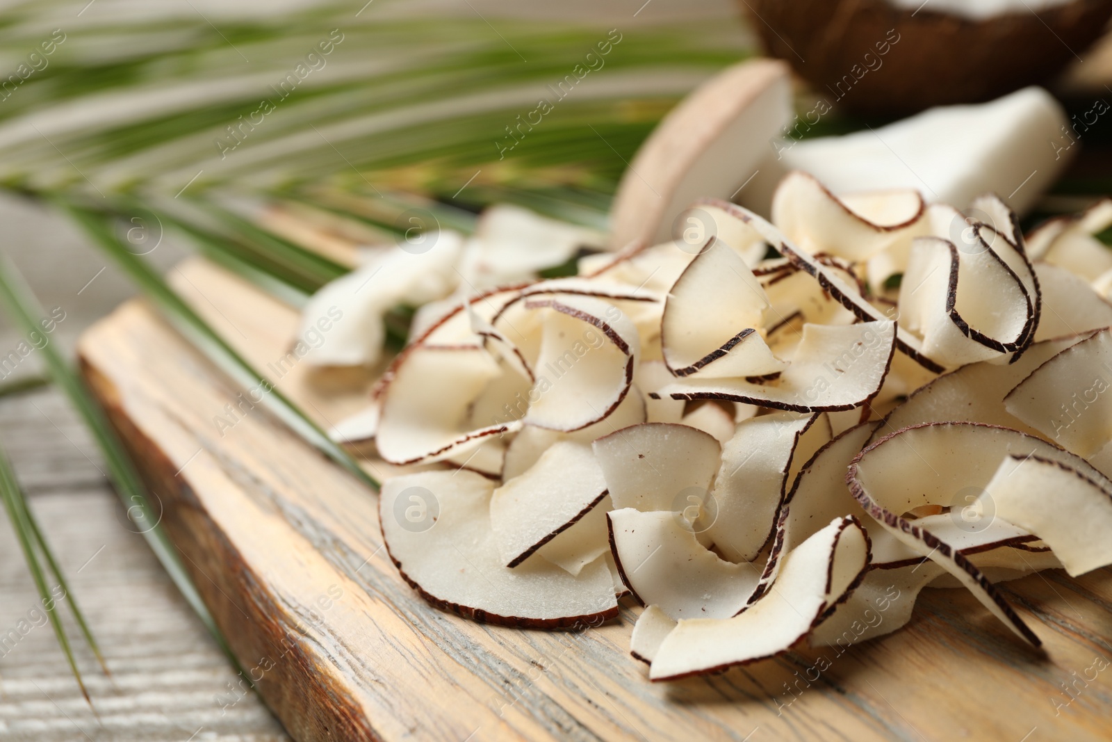 Photo of Pile of tasty coconut chips on wooden board, closeup