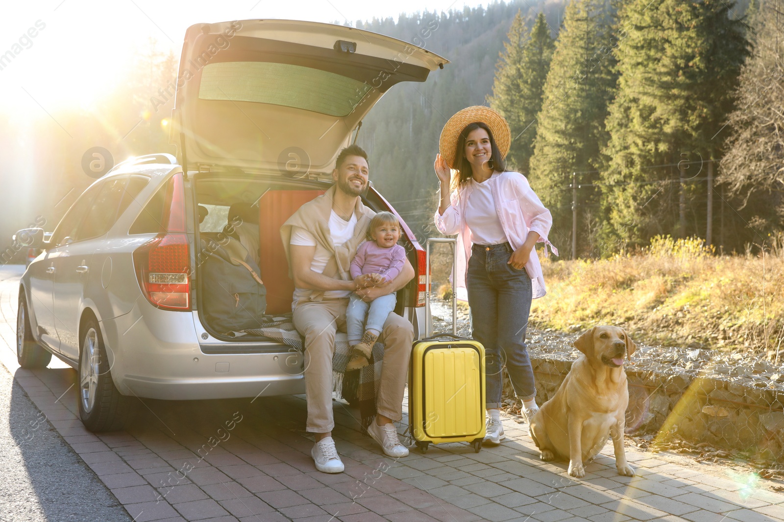 Photo of Parents, their daughter and dog near car outdoors. Family traveling with pet