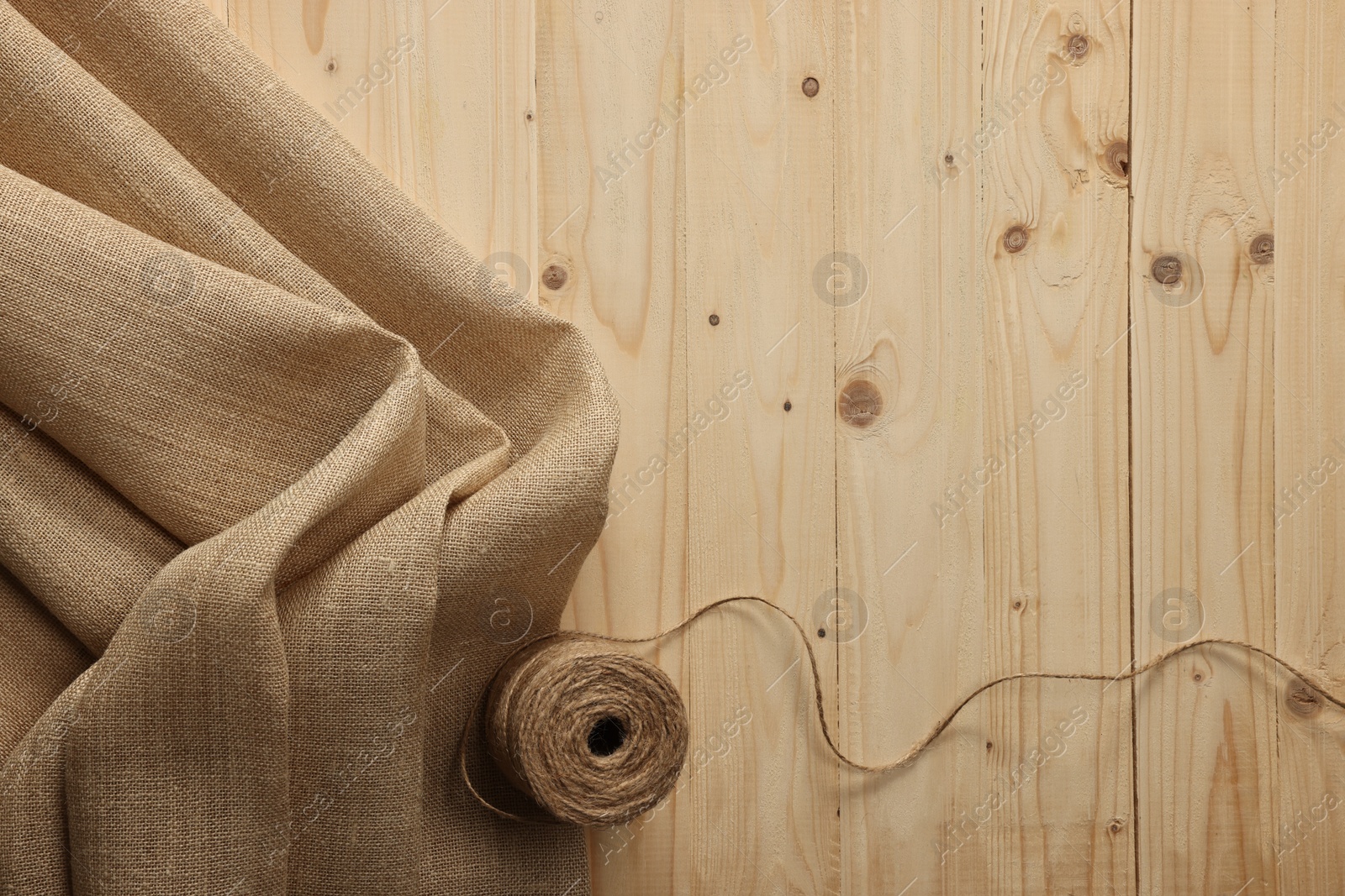 Photo of Burlap fabric and spool of thread on wooden table, top view. Space for text