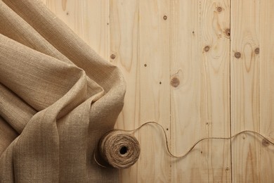 Burlap fabric and spool of thread on wooden table, top view. Space for text