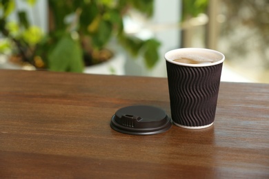 Cardboard cup of coffee on table against blurred background. Space for text