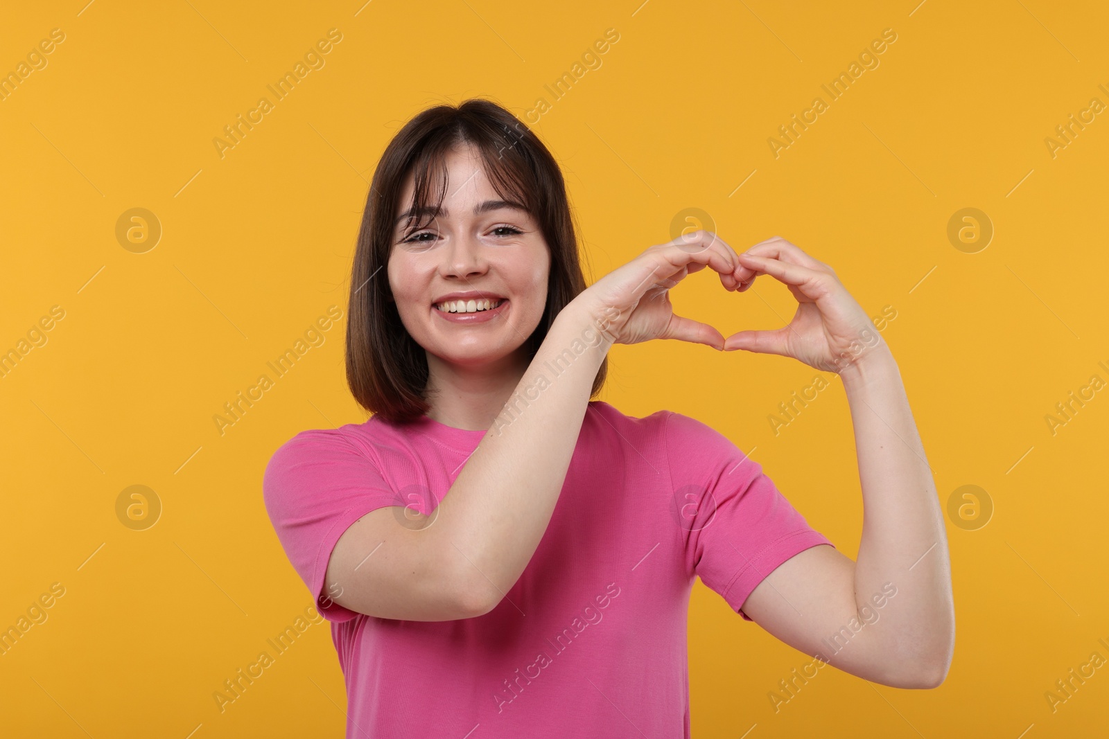 Photo of Happy woman showing heart gesture with hands on orange background