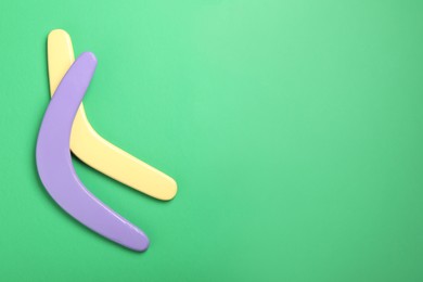 Colorful wooden boomerangs on green background, flat lay. Space for text