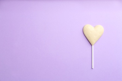 Photo of Chocolate heart shaped lollipop on light lilac background, top view. Space for text