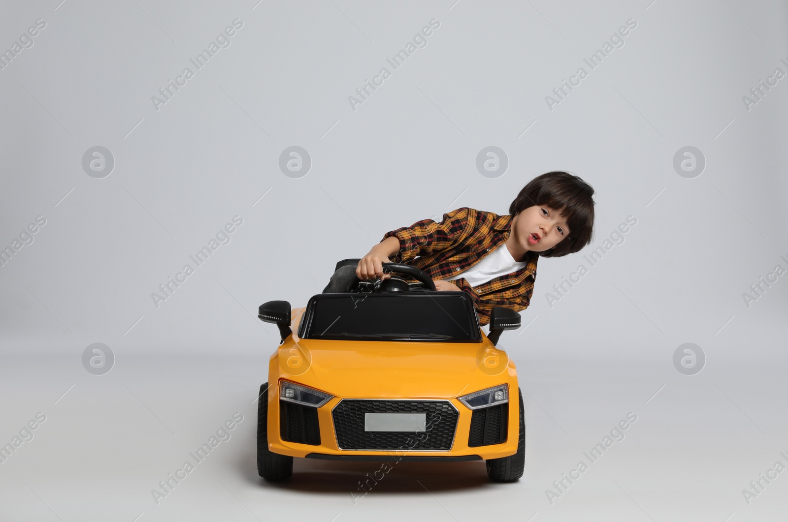 Photo of Cute little boy driving children's electric toy car on grey background