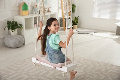 Photo of Cute little girl playing on swing at home