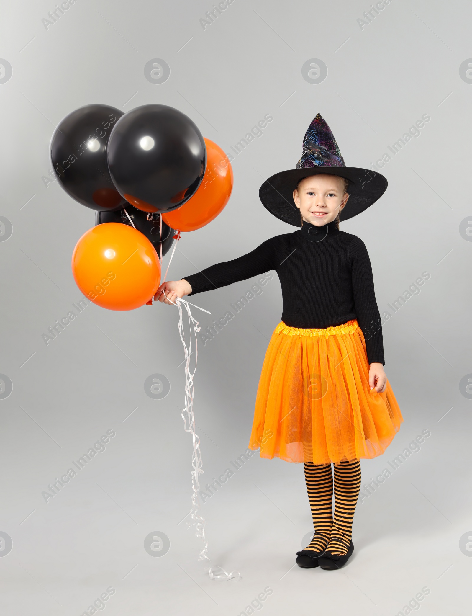 Photo of Cute little girl with balloons wearing Halloween costume on grey background