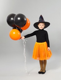 Photo of Cute little girl with balloons wearing Halloween costume on grey background