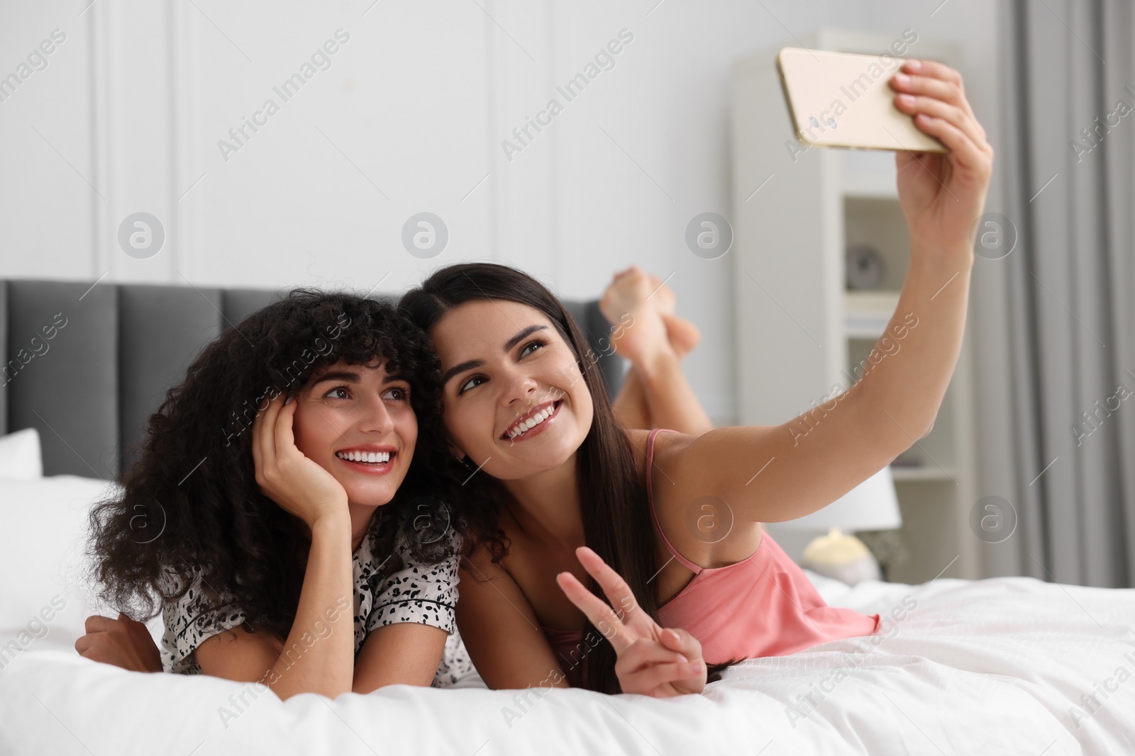 Photo of Happy young friends taking selfie on bed at home