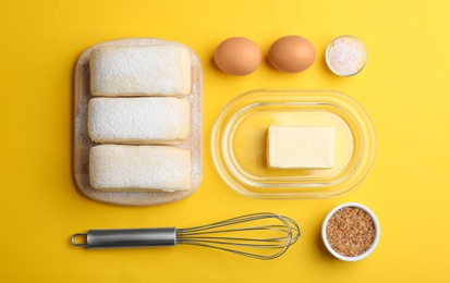 Flat lay composition of puff pastry dough and ingredients on yellow background