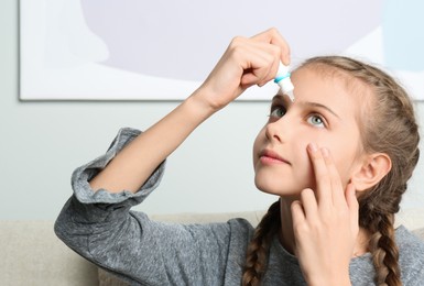 Photo of Adorable little girl using eye drops indoors