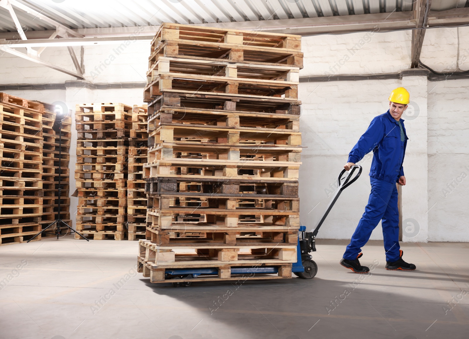 Image of Worker moving wooden pallets with manual forklift in warehouse