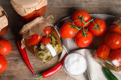 Flat lay composition with pickled tomatoes in glass jars on wooden table