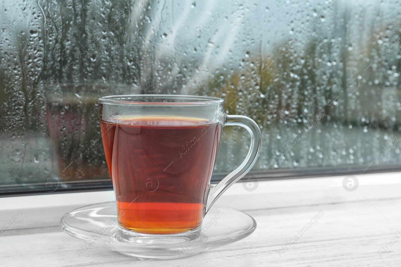 Photo of Glass cup of tea on windowsill. Rainy weather