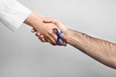 Photo of Doctor with blue ribbon on finger and patient holding hands against grey background, closeup. Symbol of medical issues
