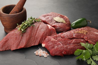 Photo of Pieces of raw beef meat, mortar with pestle and spices on black table, closeup