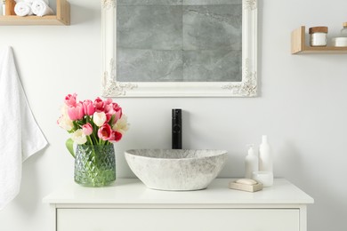 Vase with beautiful pink tulips and toiletries near sink in bathroom