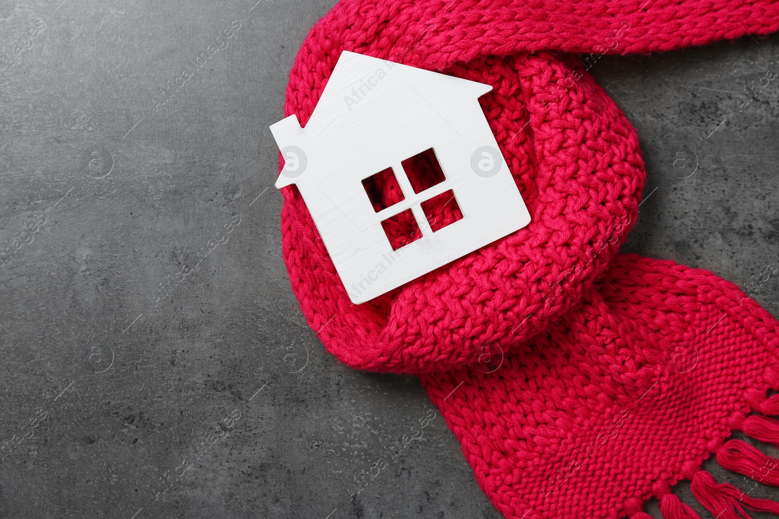 Photo of Wooden house model and red scarf on grey stone background, top view. Heating efficiency