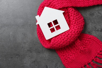 Photo of Wooden house model and red scarf on grey stone background, top view. Heating efficiency