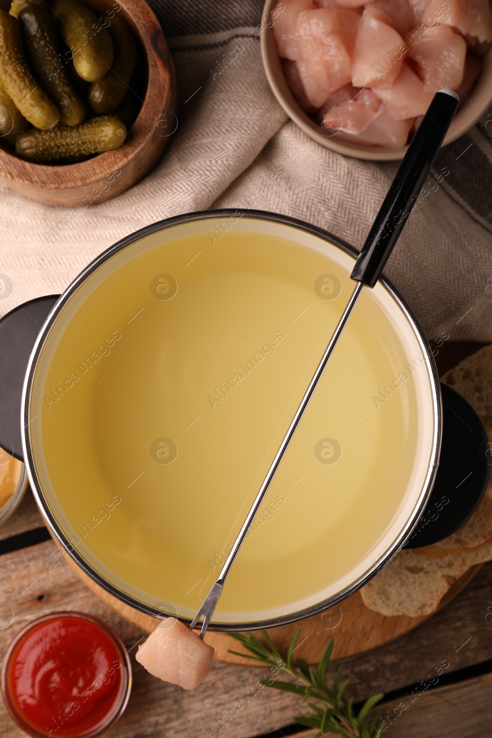 Photo of Fondue pot with oil, fork, raw meat pieces and other products on wooden table, flat lay