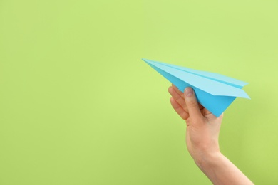Photo of Woman holding paper plane on green background, closeup. Space for text