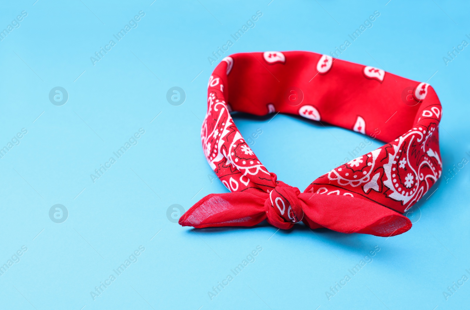 Photo of Tied red bandana with paisley pattern on light blue background, space for text