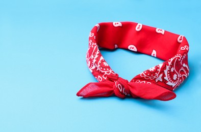 Tied red bandana with paisley pattern on light blue background, space for text