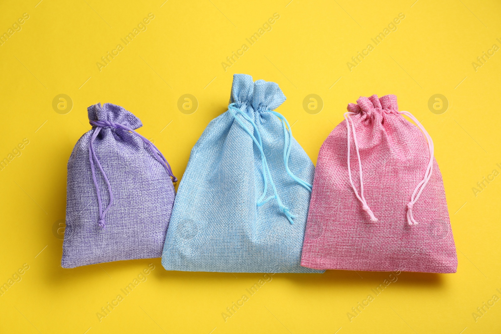 Photo of Colorful burlap bags on yellow background, flat lay