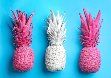 White and pink pineapples on light blue background, flat lay. Creative concept