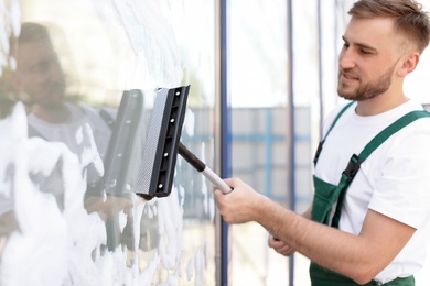 Male cleaner wiping window glass with squeegee from outside