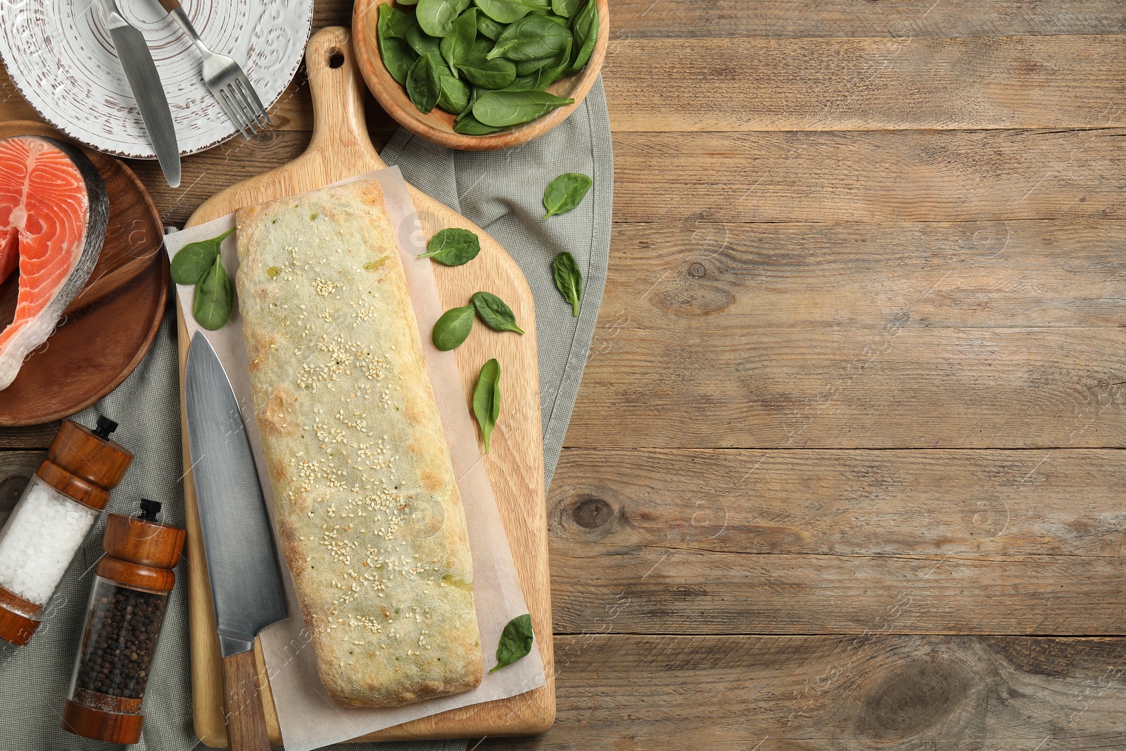 Photo of Delicious strudel with salmon and spinach on wooden table, flat lay. Space for text