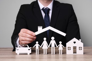 Photo of Man holding figure of roof above family at wooden table. closeup. Insurance concept
