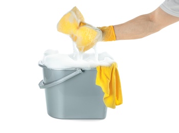 Man holding sponge over bucket with foam on white background, closeup. Cleaning supplies