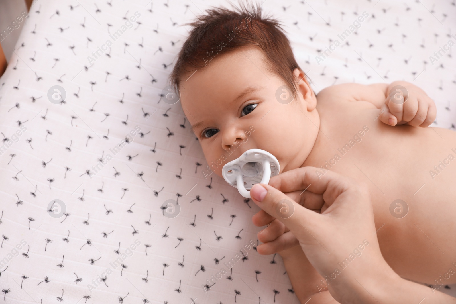 Photo of Mother giving pacifier to her cute little baby on blanket, top view