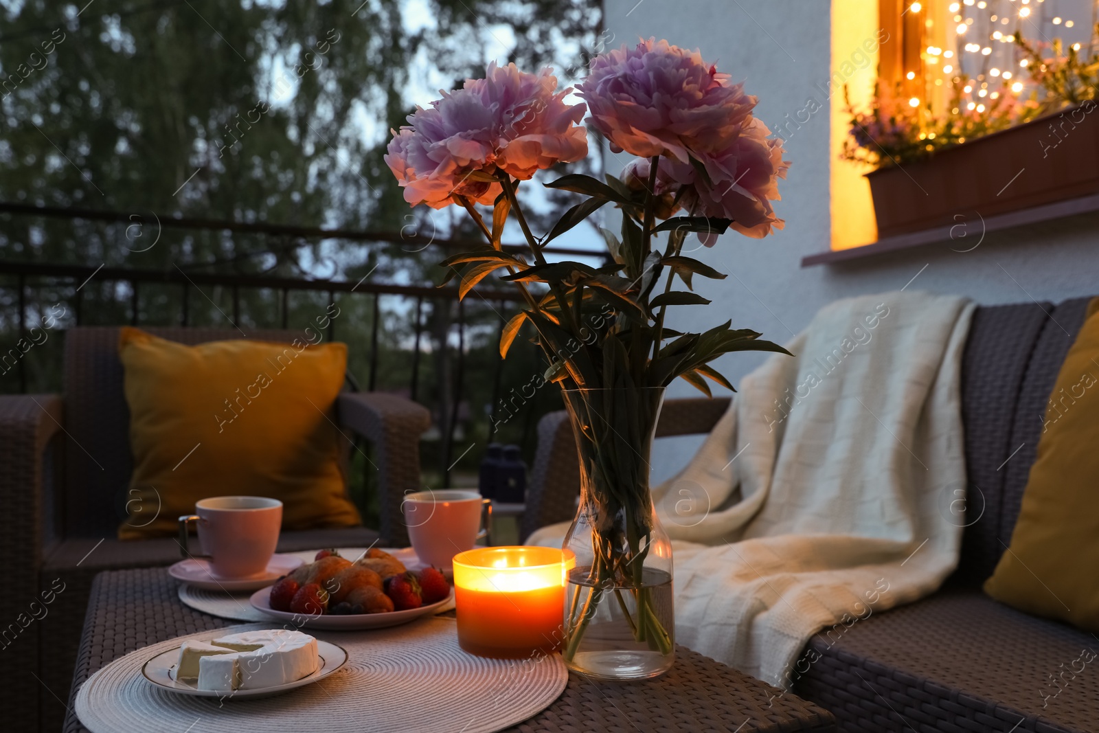 Photo of Rattan table with drink, food, flowers and candle on outdoor terrace in evening