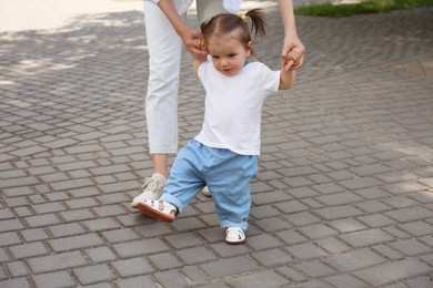 Photo of Mother supporting daughter while she learning to walk outdoors, closeup