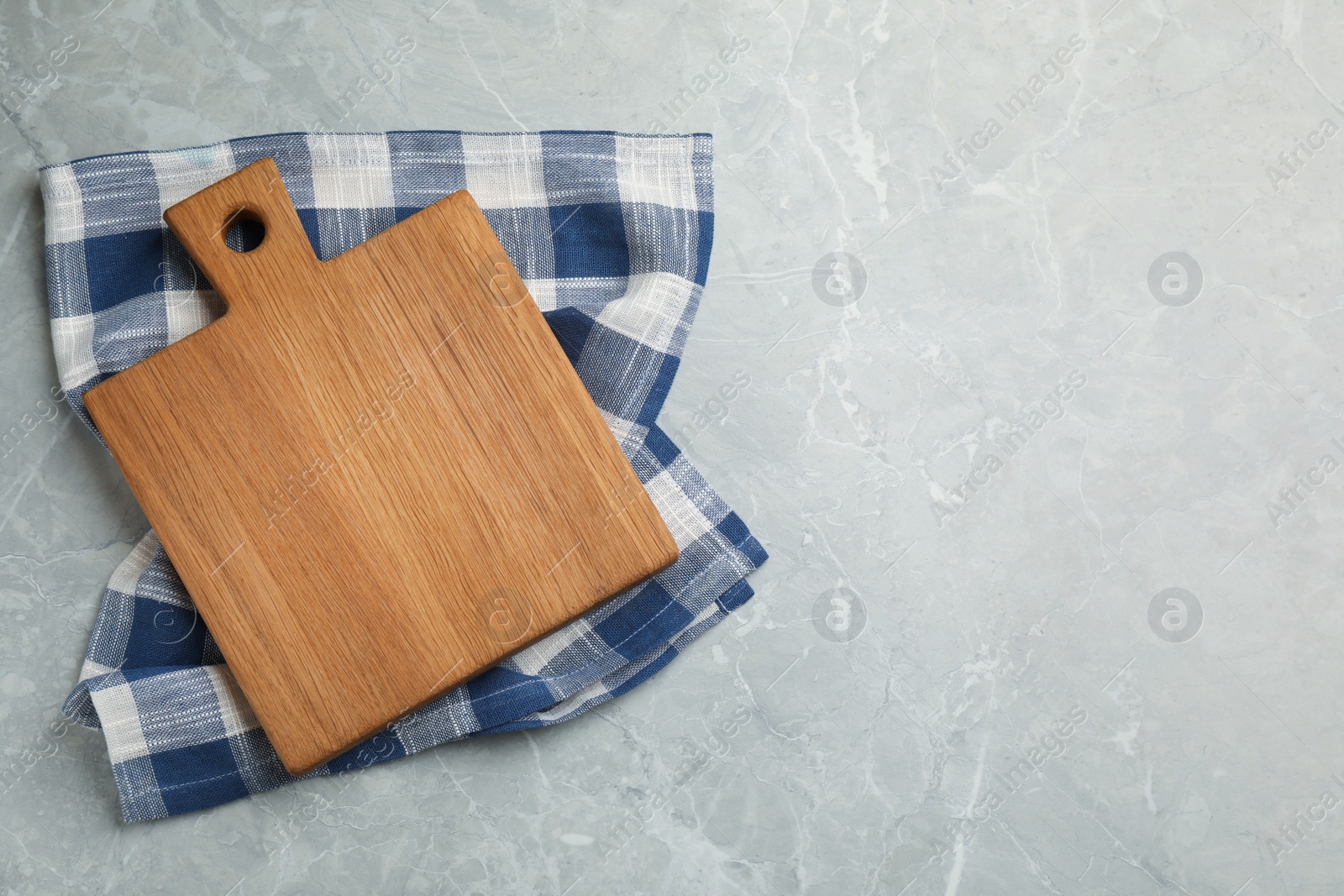 Photo of Kitchen towel and wooden cutting board on grey table, top view. Space for text