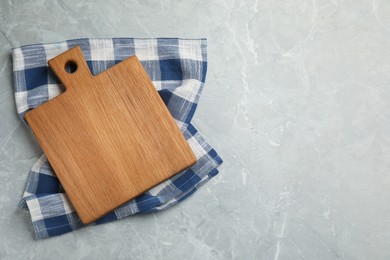 Kitchen towel and wooden cutting board on grey table, top view. Space for text