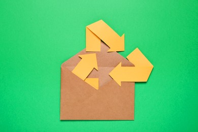 Photo of Open envelope and recycling symbol on green background, top view
