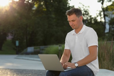 Photo of Handsome man using laptop on bench outdoors. Space for text