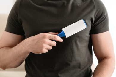 Photo of Man cleaning grey t-shirt with lint roller on light background, closeup
