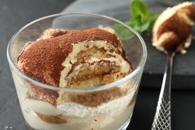 Photo of Delicious tiramisu in glass and spoon on black table, closeup