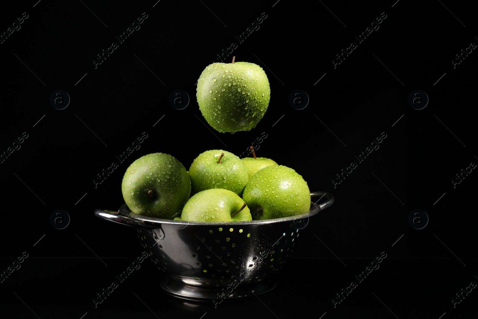 Photo of Green apple with water drops falling down into colander on black background